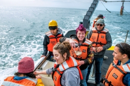 students wearing safety gear on a research vessel with turbulent waters