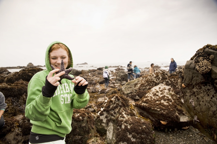 student with a green hoodie on holding a starfish with rocks in the background